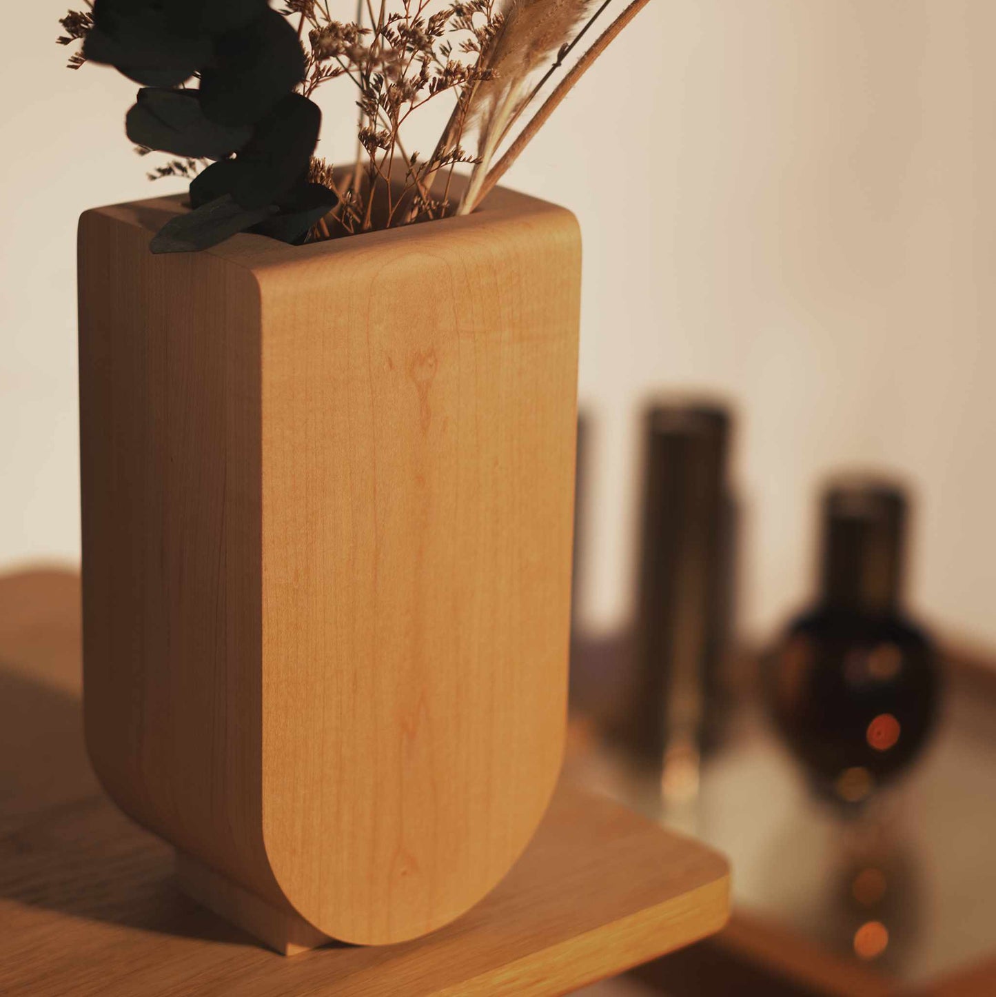 Handcrafted wooden vase with dried plants in it on a wooden surface with a blurred background