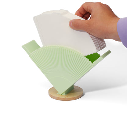 mint green coffee filter stand against a white background with a hand refilling it with cone-shaped coffee filters
