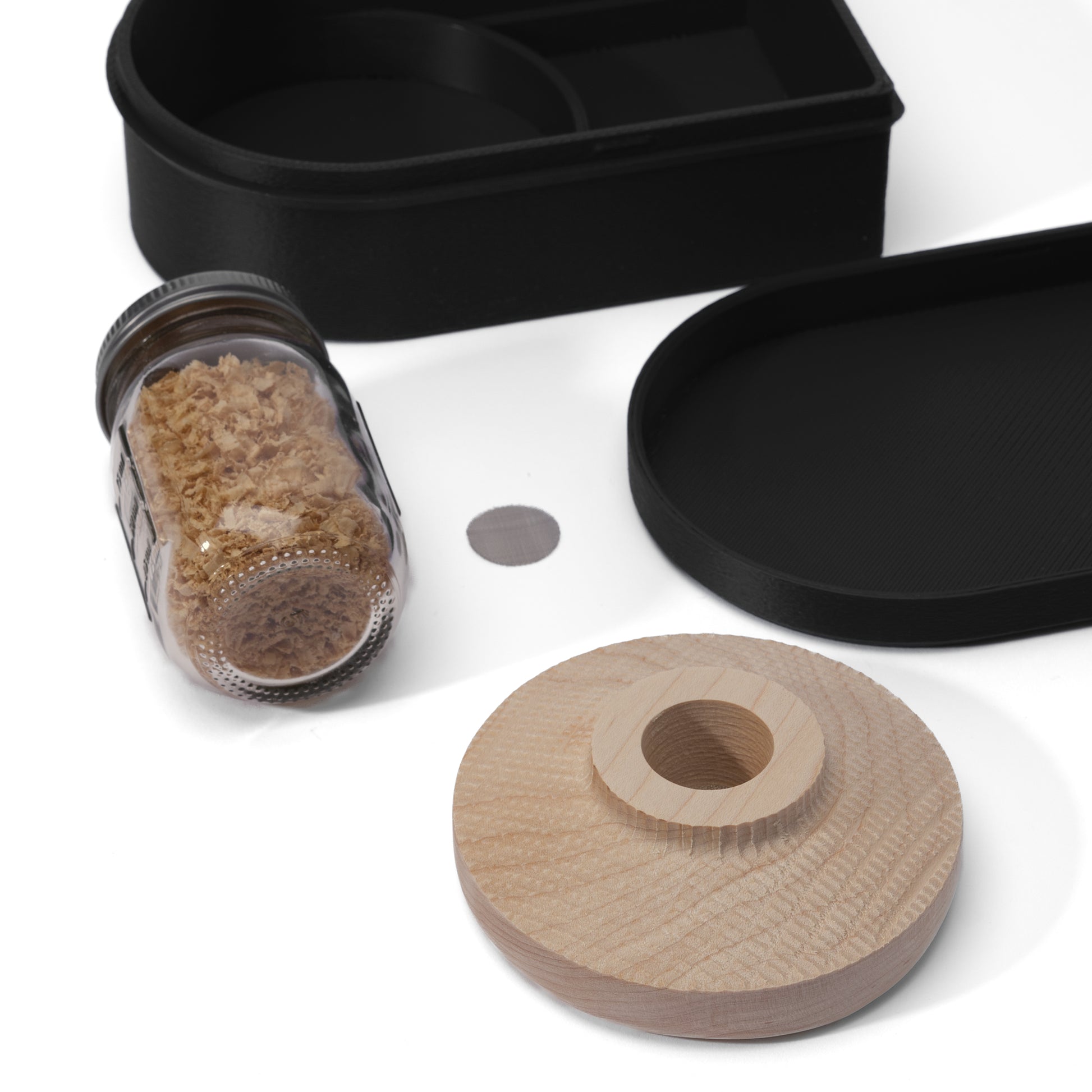 Black 3D Printed container, wooden cocktail smoker, jar of white oak wood shavings, stainless steel mesh filter, and a lid for the container displayed on a white background
