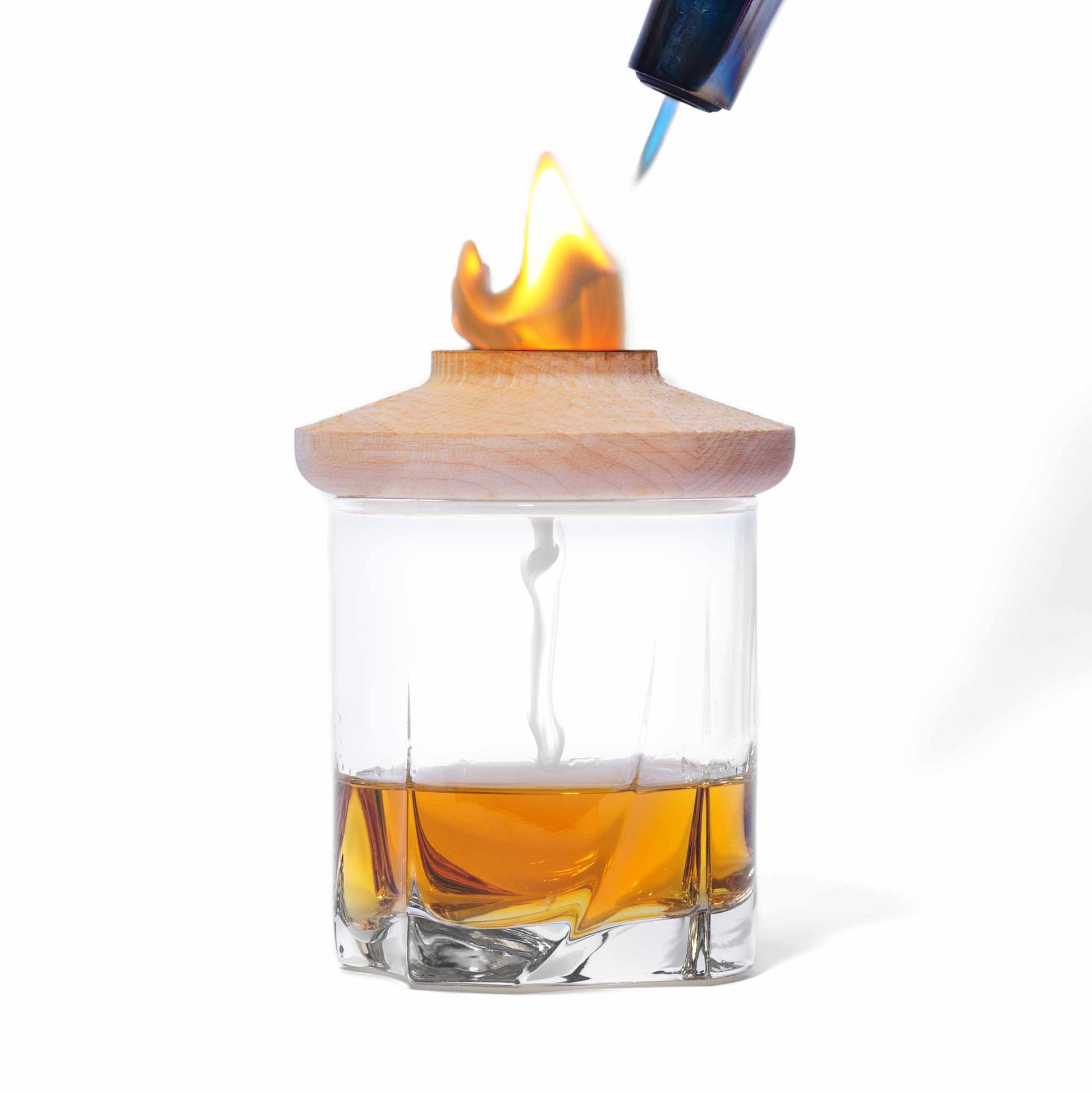 Glass of whiskey with wooden cocktail smoker on top being lit displayed on a white background