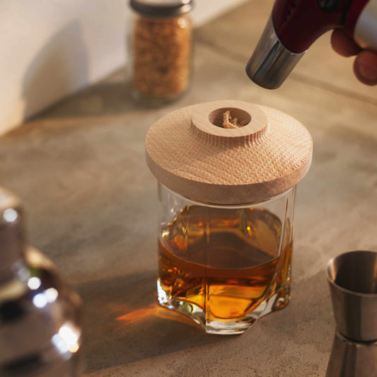 Glass of whiskey with wooden cocktail smoker on it on top of a concrete surface