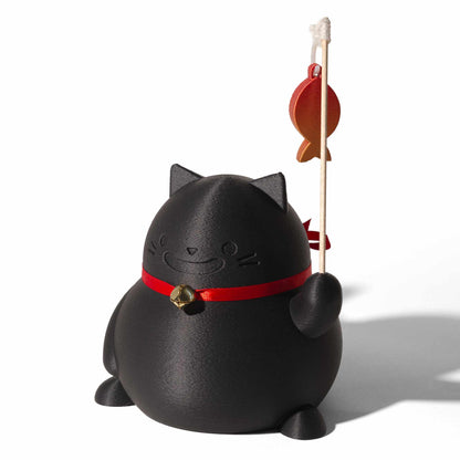 A black lucky cat decorative object with a red collar and small gold bell, holding a wood stick with an orange fish ornament, against a white background
