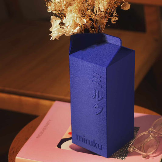 blue 2L milk carton vase holding dried flowers displayed on book
