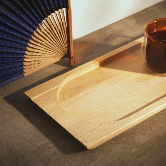 Handmade wood tray with a coffee glass on it next to a blue fan on top of a concrete surface
